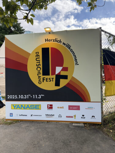 2025年のドイツフェスティバル（DEUTSCHLAND FEST）の案内看板。ドイツ国旗の色（黒・赤・黄）を用いたロゴと、「2025.10.31 Fri. - 11.3 Mon.」の日程、YANASEやHARIBOなどの協賛企業ロゴが記載されています。